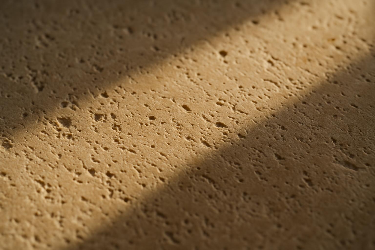 Close-up of pitted cream travertine stone with sunlight across the surface