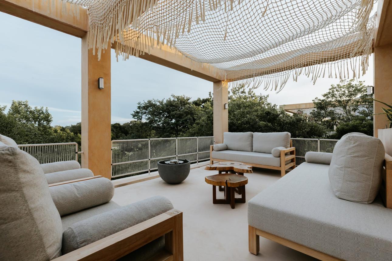 Rooftop terrace under a macramé canopy with teak lounge furniture and root-wood coffee tables
