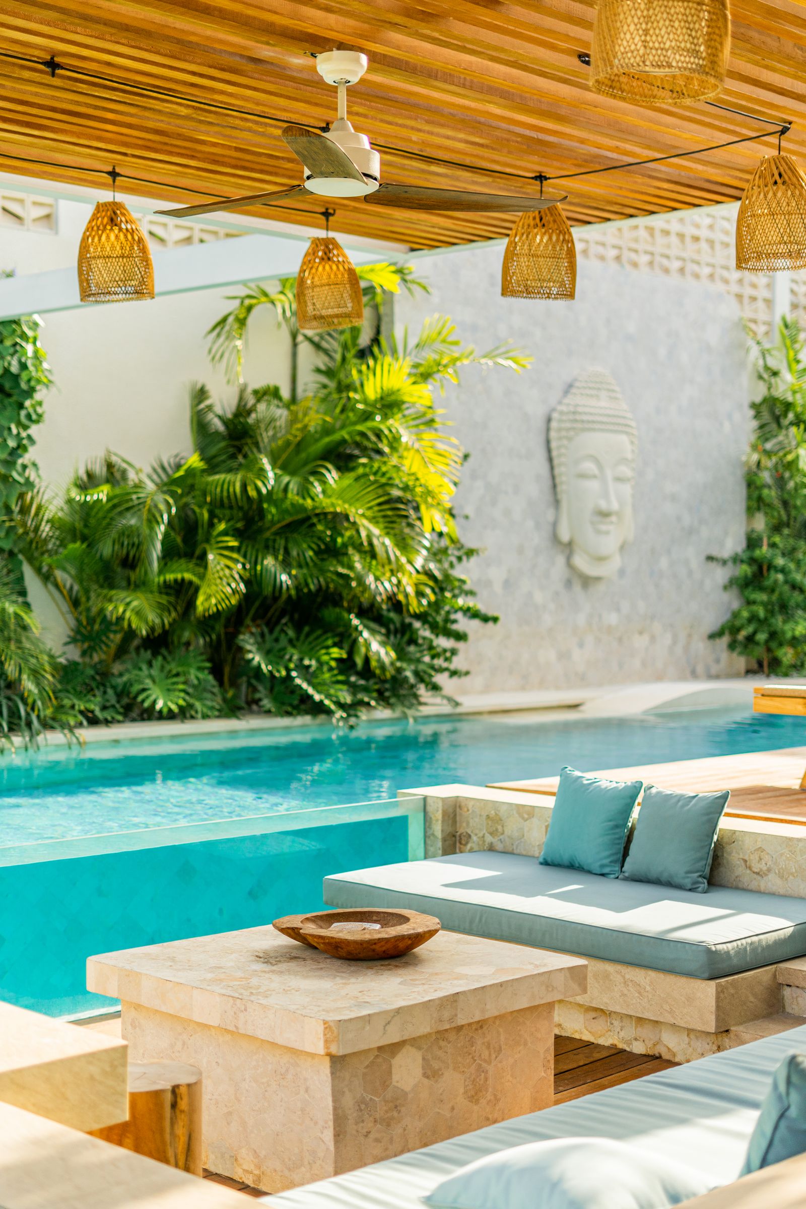 Pool terrace with a stone daybed and cushions among tropical plants under rattan lights