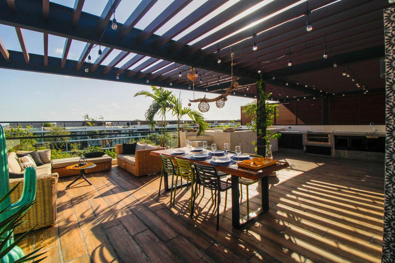 Rooftop terrace under a slatted steel pergola with string lights and a dining table