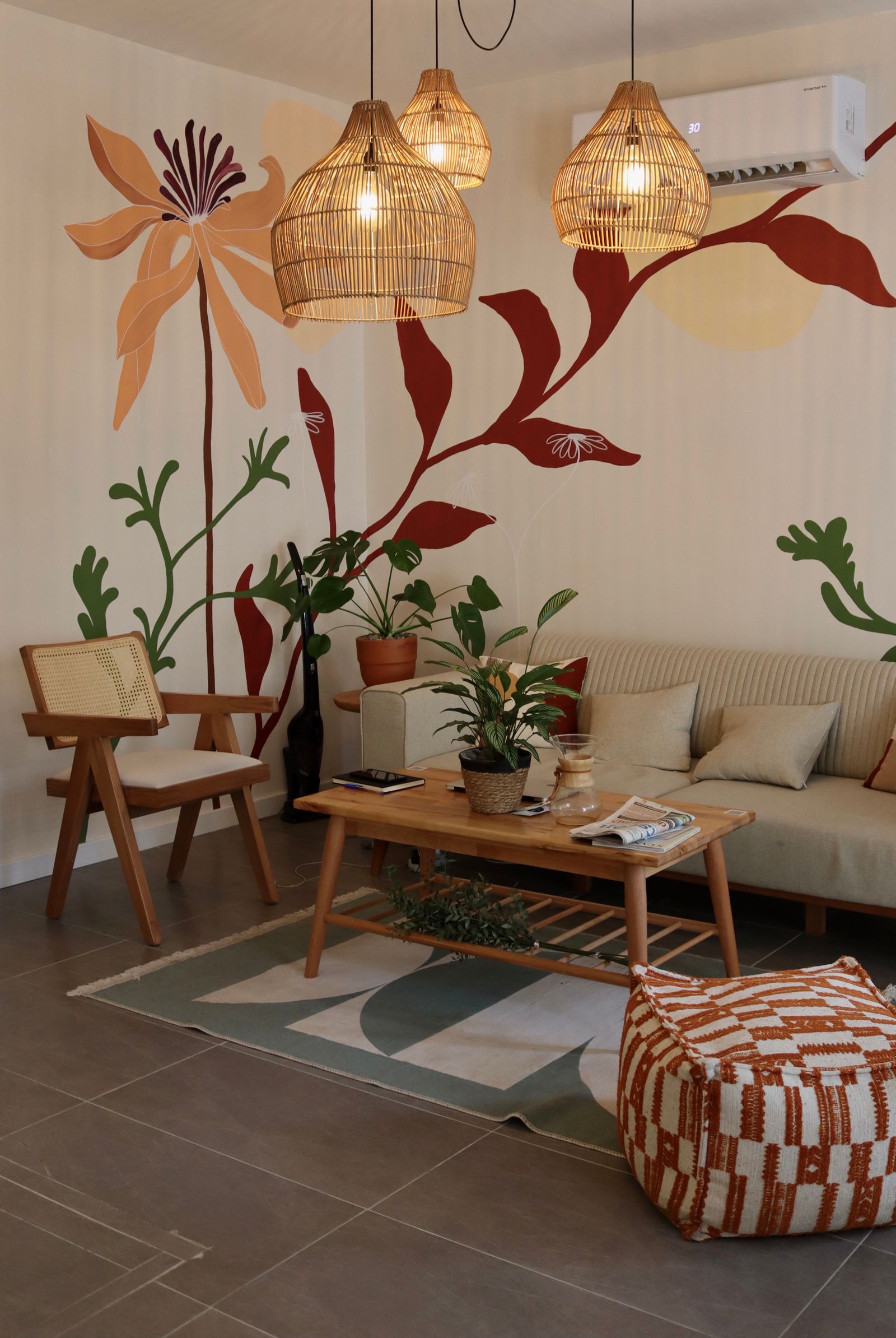 Living room with rattan pendant lamps, a patterned pouf and a floral wall mural