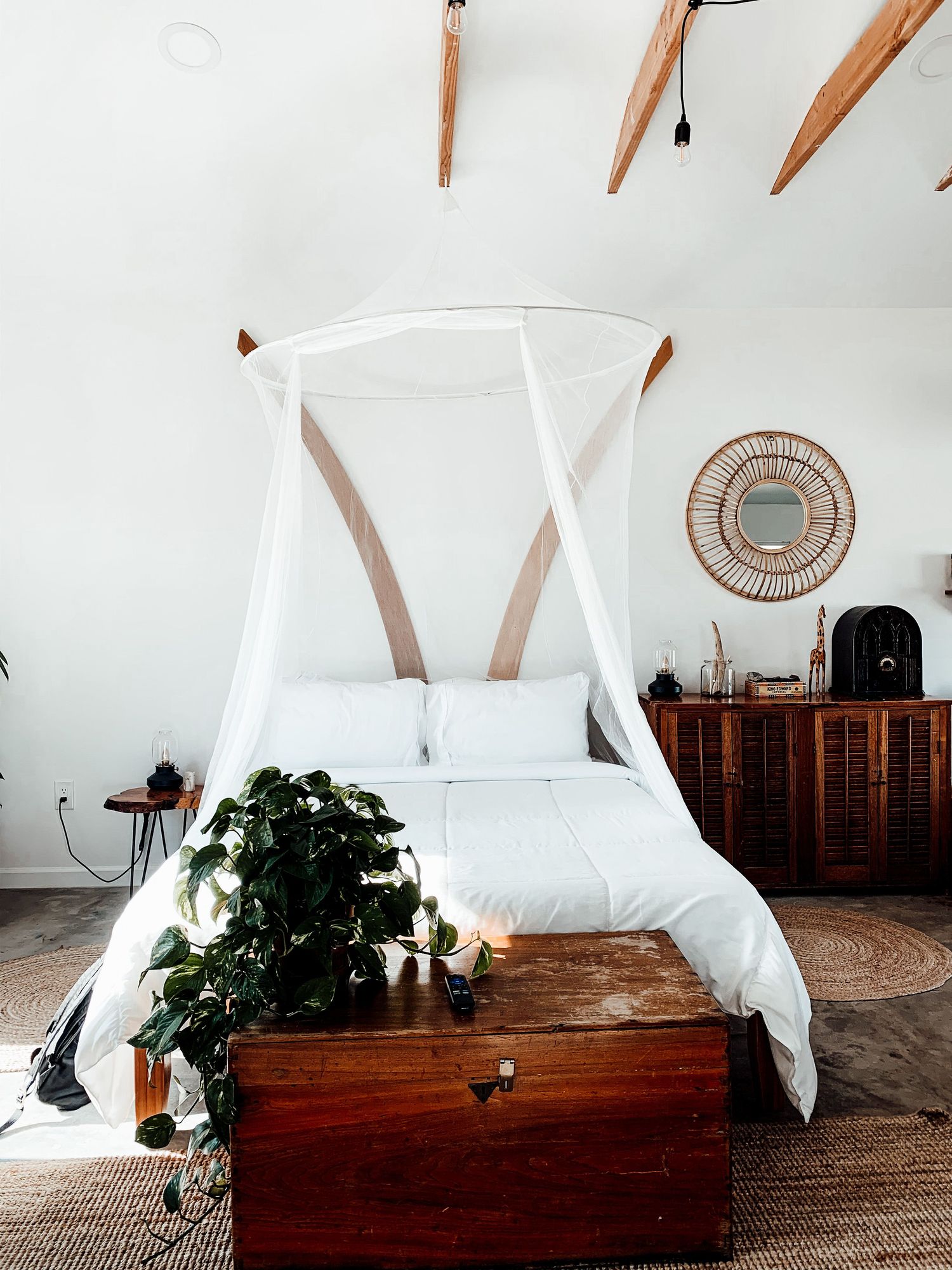 Canopy bed with sheer netting, a carved wood chest and woven decor