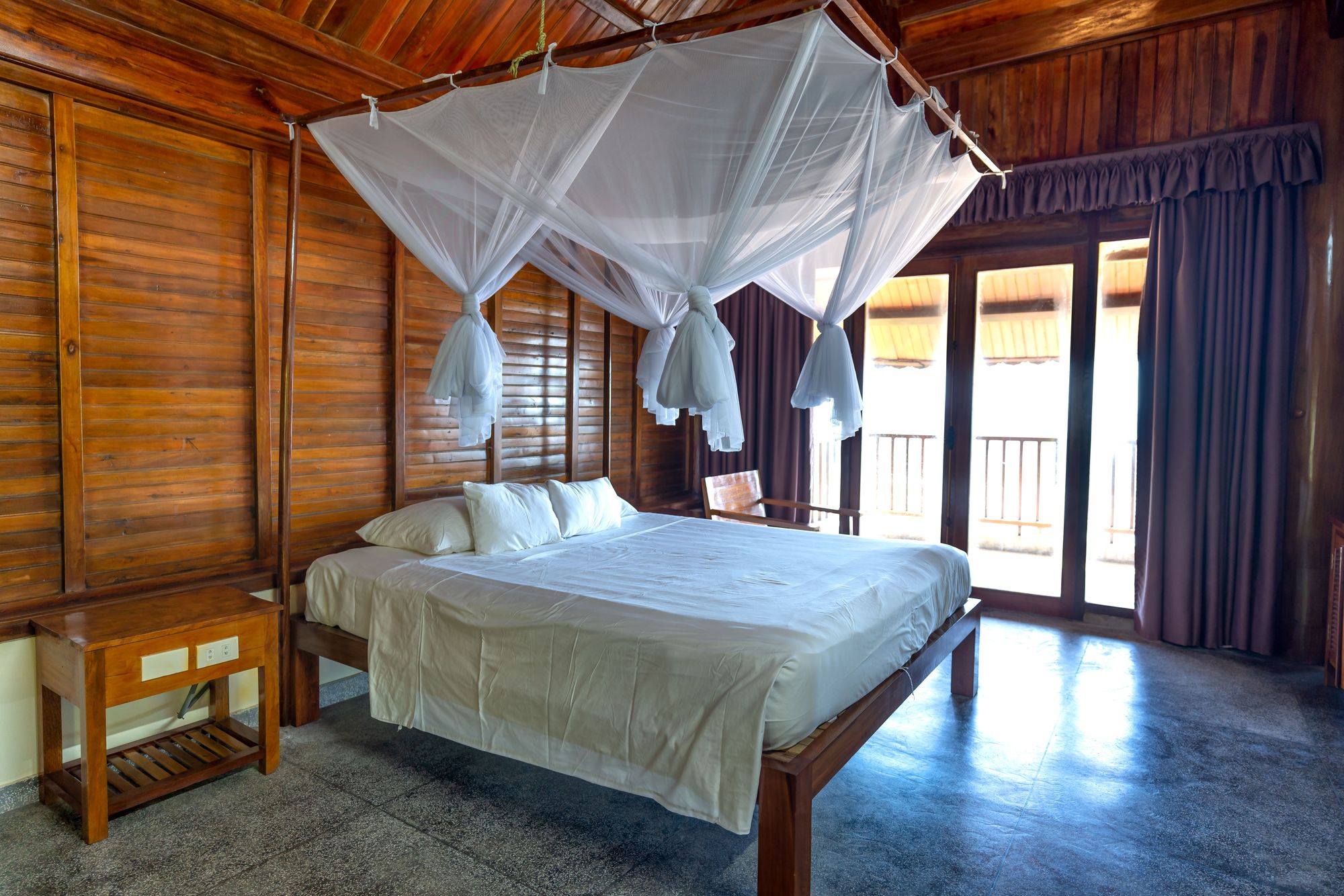 Teak-paneled bedroom with a solid-wood platform bed under a mosquito-net canopy