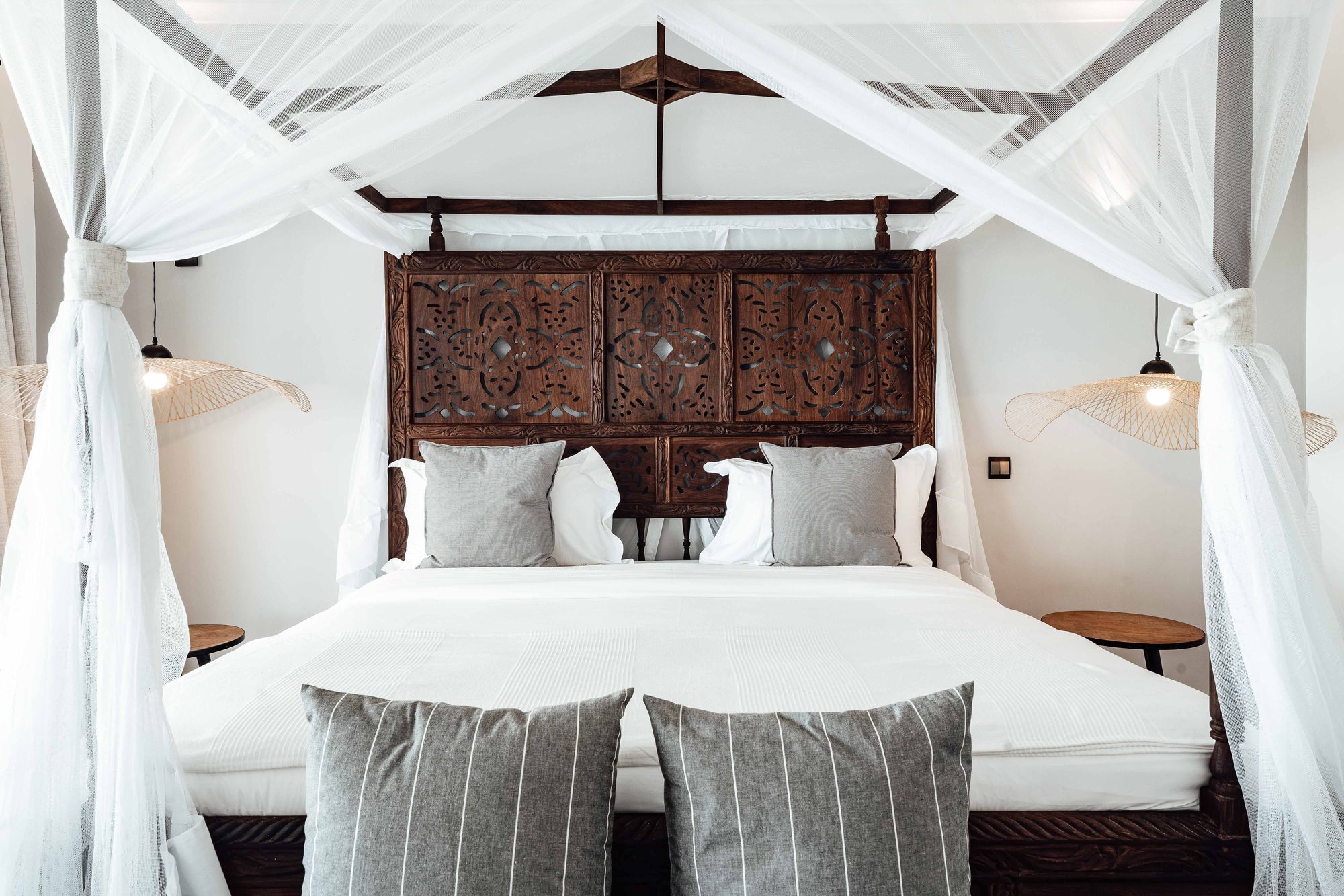 Canopy bed with a carved wood headboard and white linen