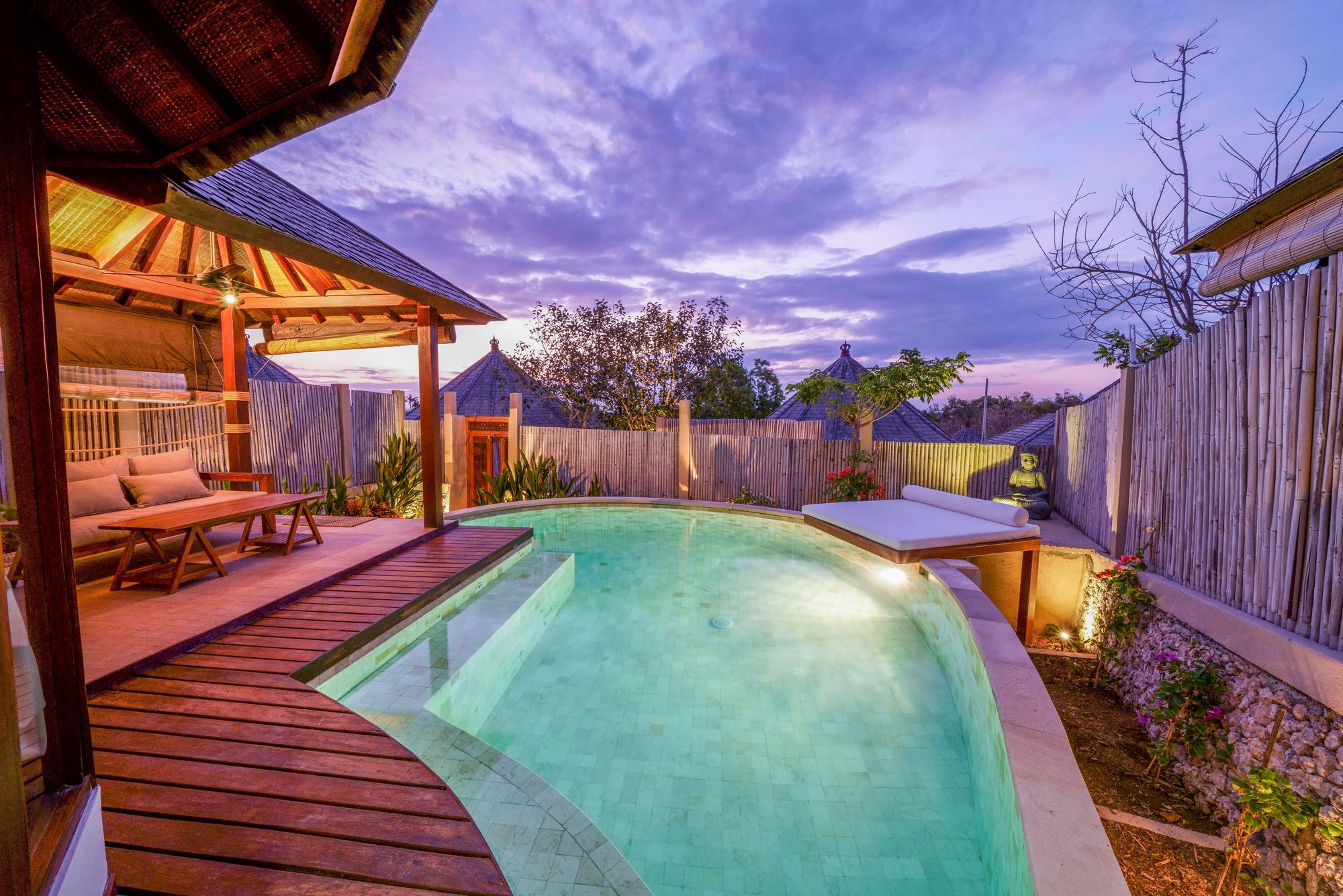 Pool deck with wooden loungers and a palapa at dusk