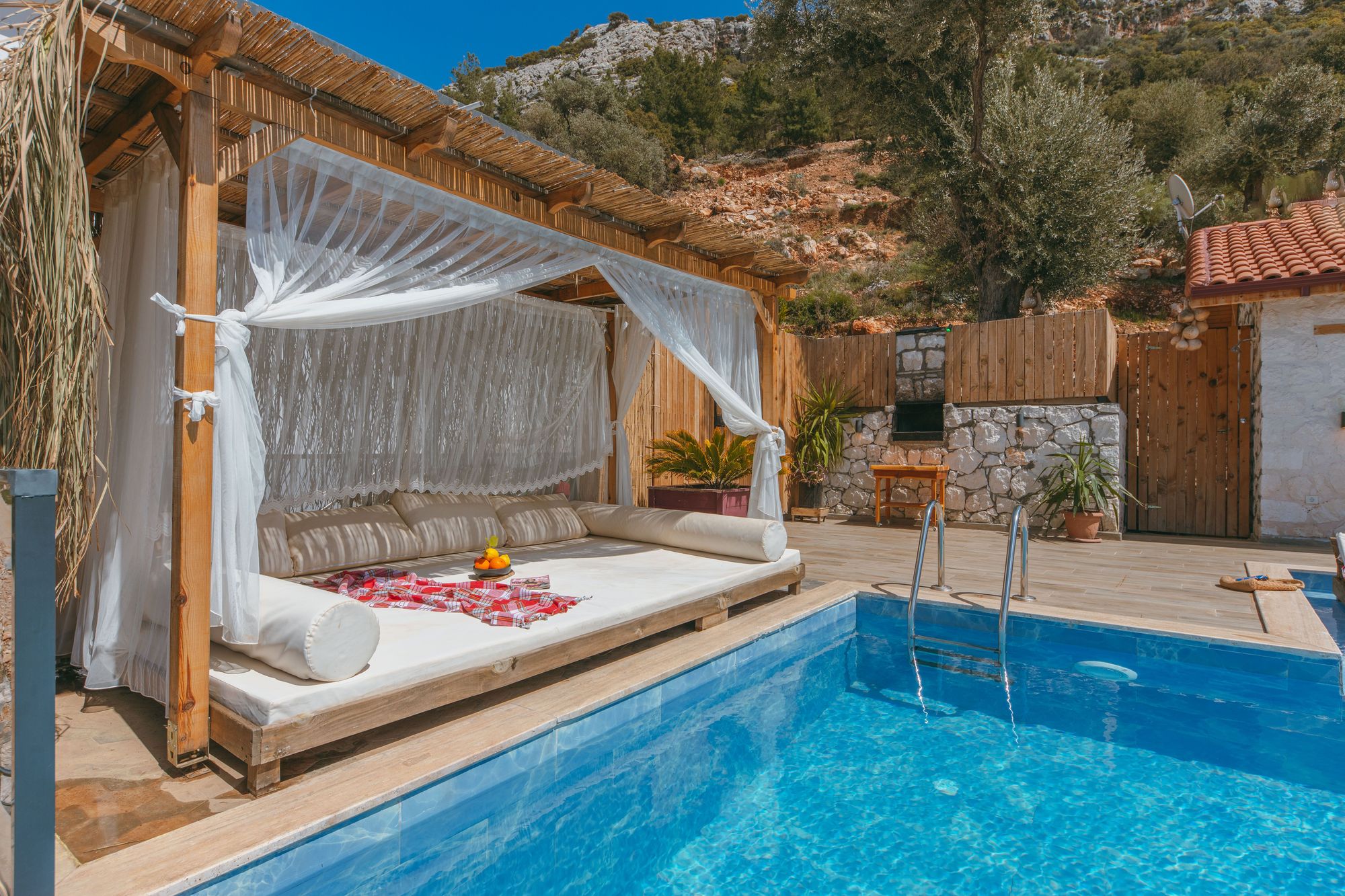 Canopy daybed beside a pool under a reed shade