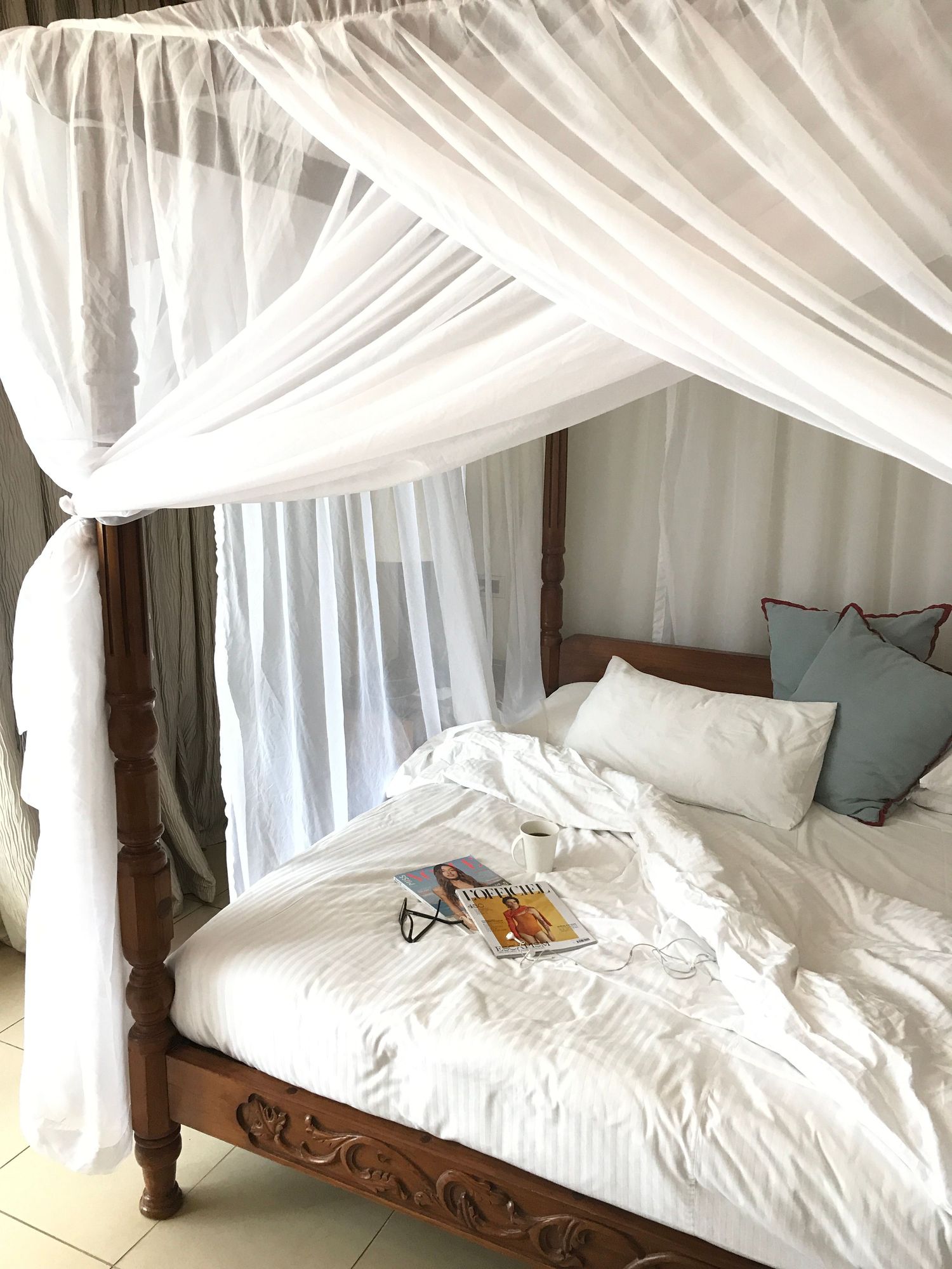 Carved wood four-poster bed with a sheer white canopy