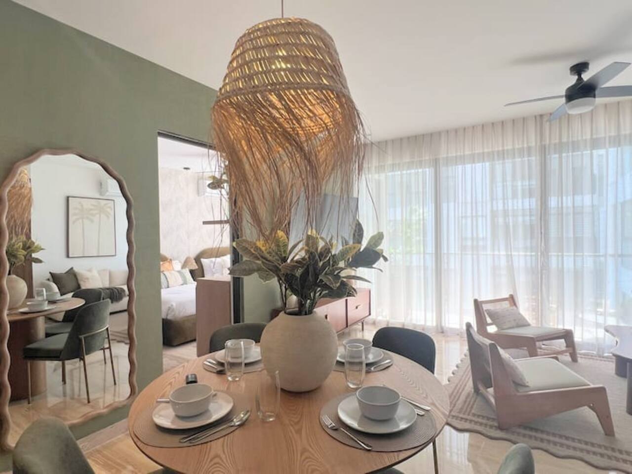 Condo in Zazil-ha, Playa del Carmen: round wood dining table under a woven palm pendant, sage wall, linen curtains and rattan lounge chairs